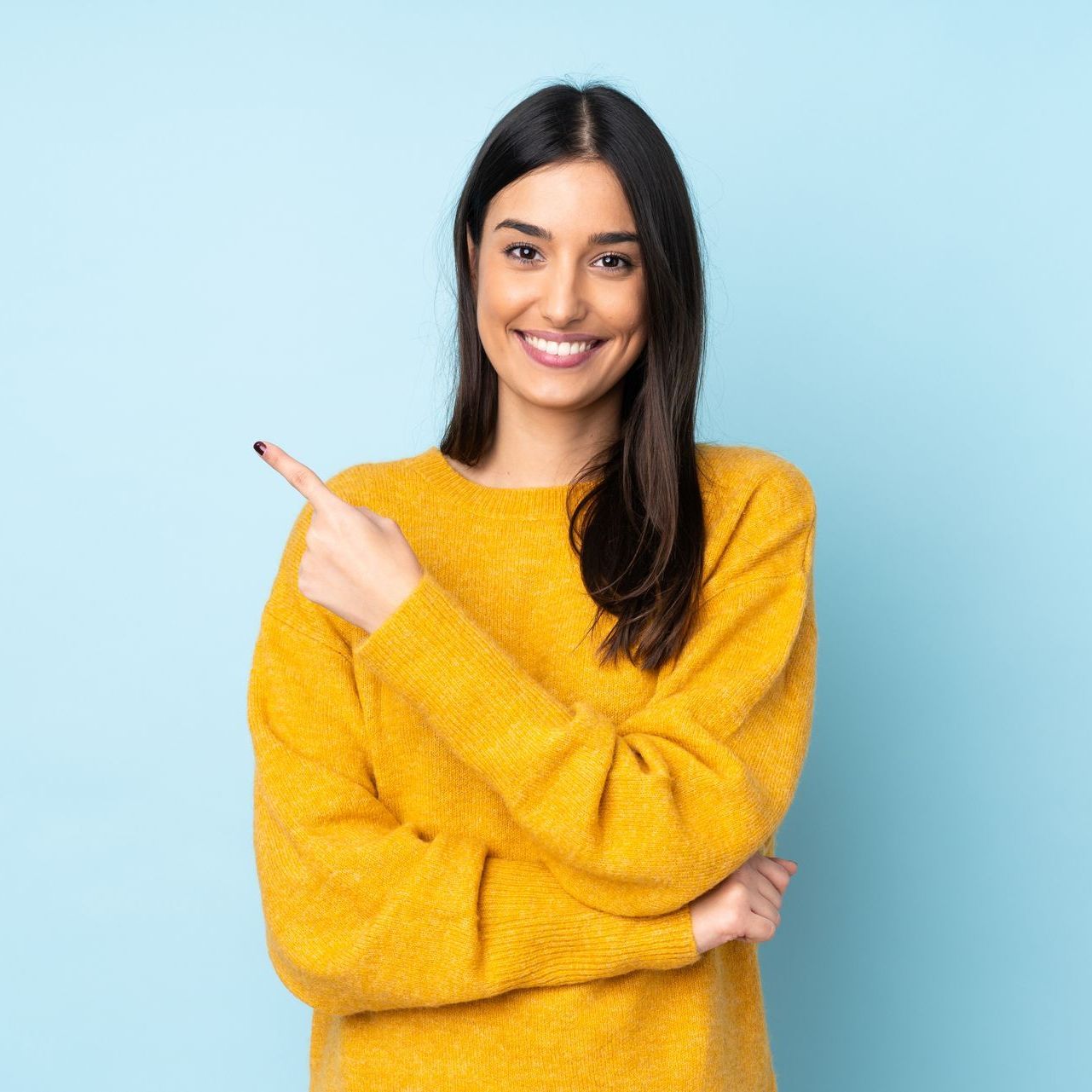 A woman in a yellow sweater is smiling and pointing to the side.