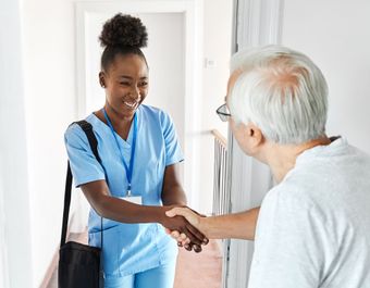 A nurse is shaking hands with an elderly man in a hallway.