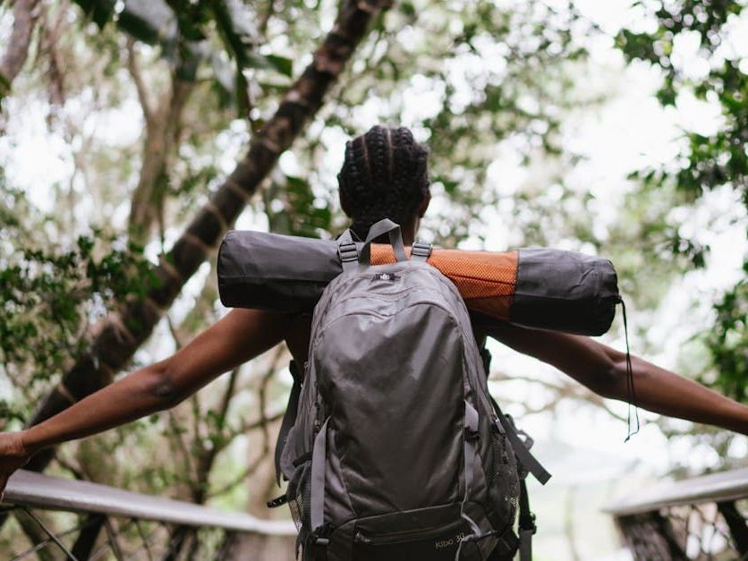 A woman with a backpack is standing on a bridge with her arms outstretched.
