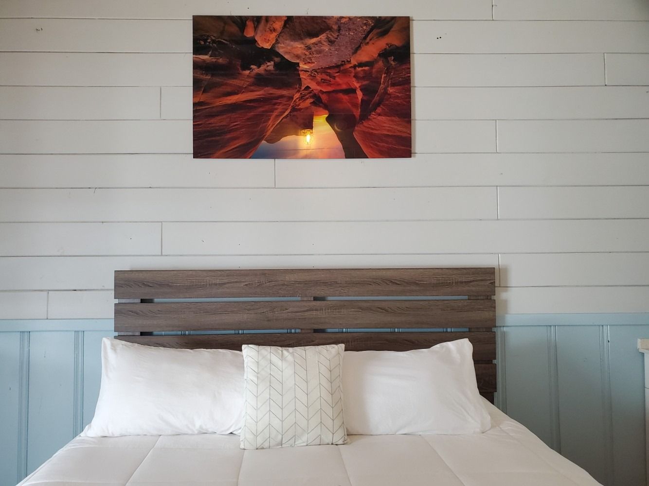 Bedroom with bed, white bedding, headboard, and photo of rock formations. Light blue and white wall.
