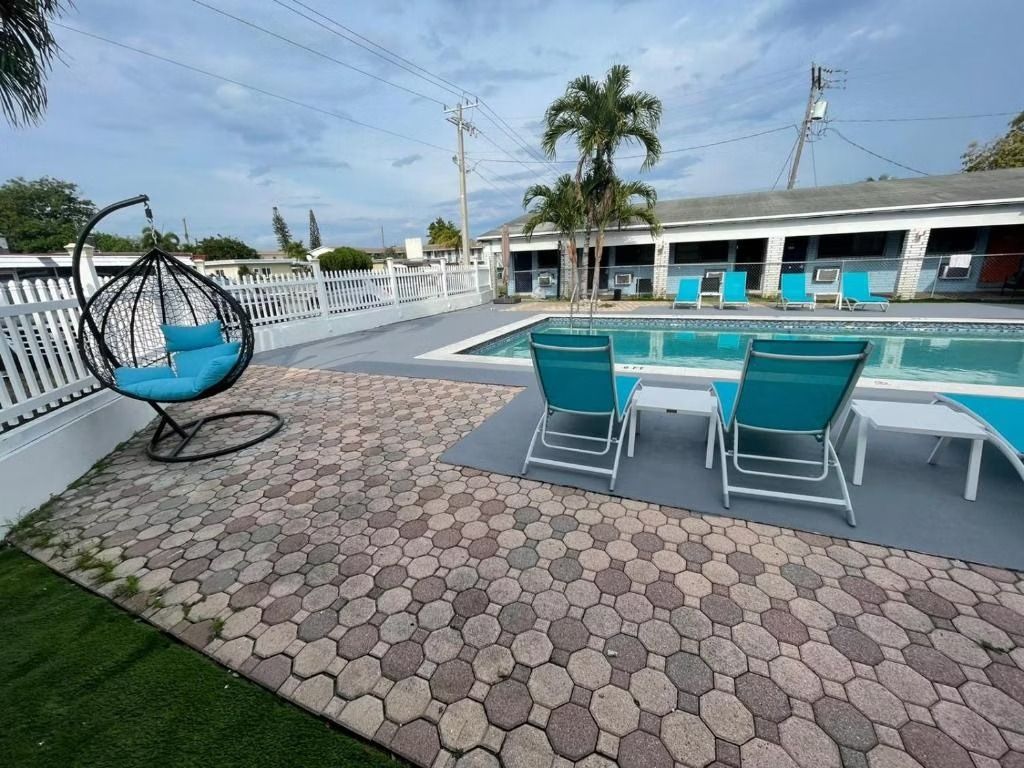 Poolside scene with lounge chairs, a hanging chair, and a building under a cloudy sky.
