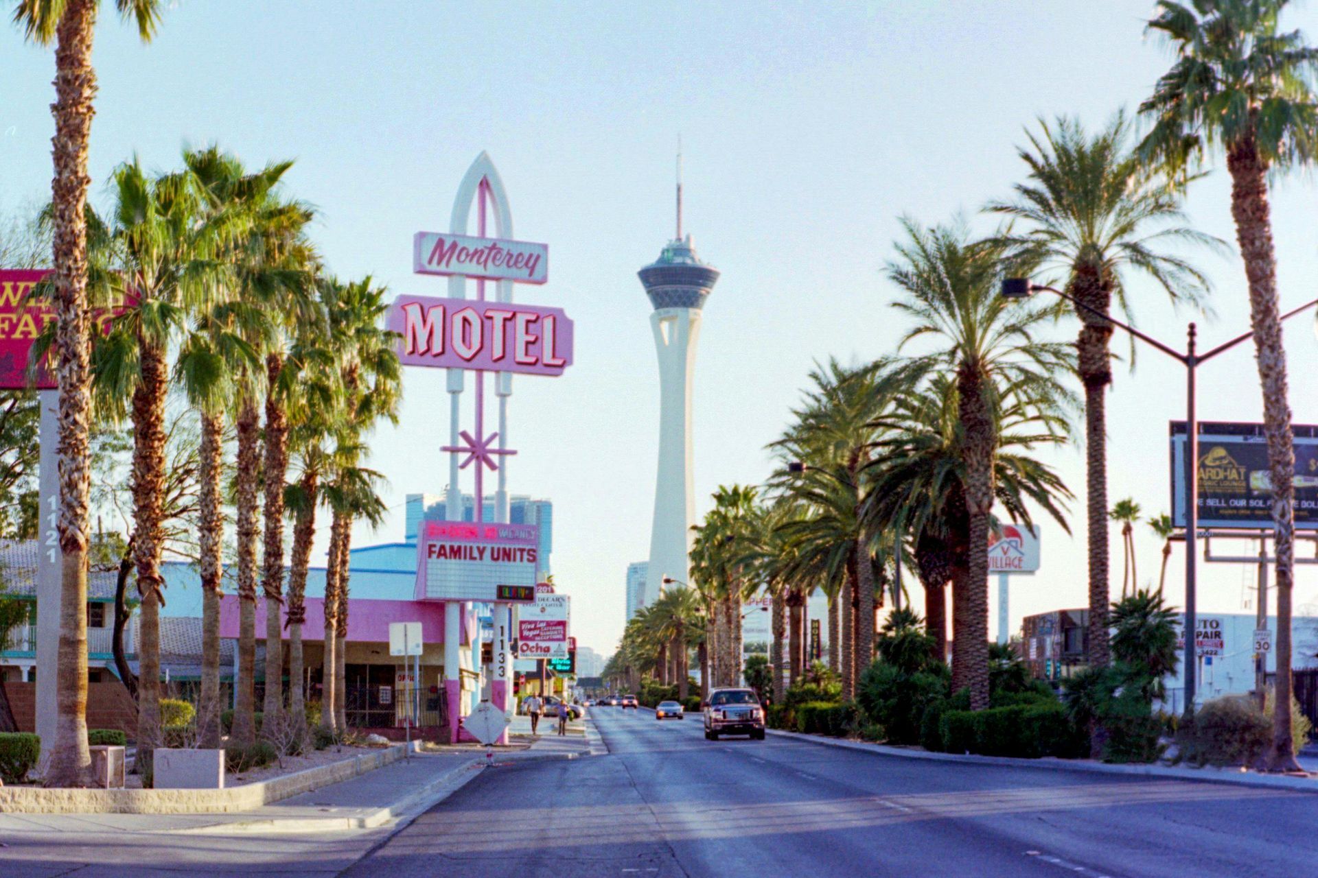 Street scene in Las Vegas, Nevada, featuring a retro motel sign, palm trees, and the Stratosphere Tower.