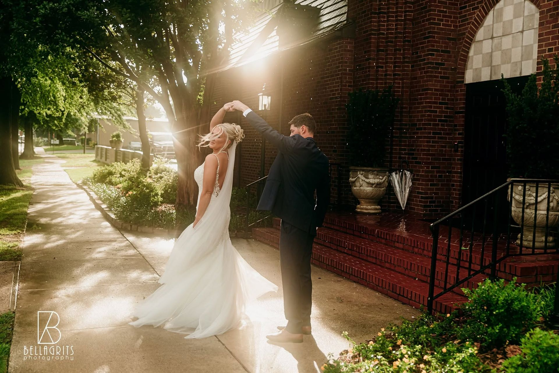 Bride in white dress, holding bouquet, poses by a fountain in front of a brick building.