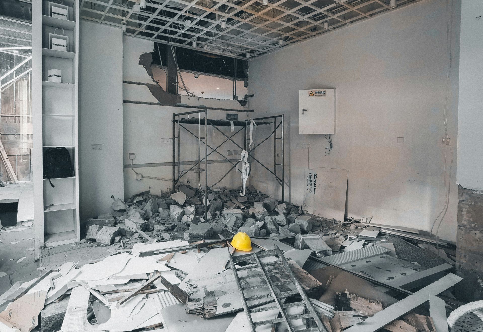 An interior room under construction with a large pile of rubble, a scaffolding frame, and a yellow hard hat on the floor.