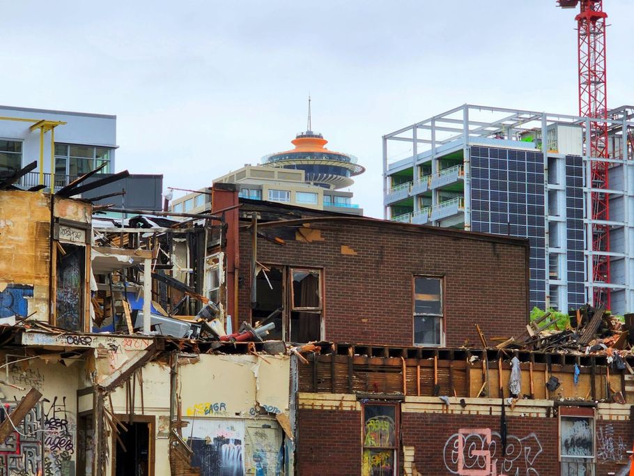 A partially demolished brick building covered in graffiti, with the Vancouver Lookout tower visible in the background.