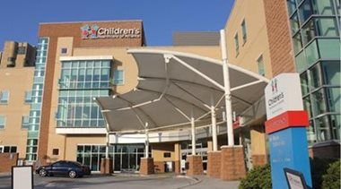 Children’s hospital entrance with white canopy, brick buildings, and blue glass facade