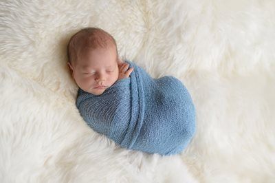 Sleeping newborn wrapped in a blue blanket on a soft white fur blanket