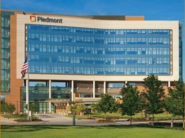 Piedmont hospital building with blue glass facade, American flag, and trees in front