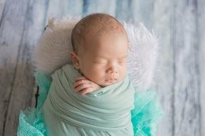 Sleeping baby swaddled in mint green on a soft white furry blanket