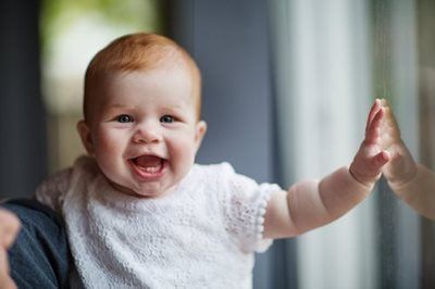 Smiling baby in a white shirt reaching a hand toward the camera