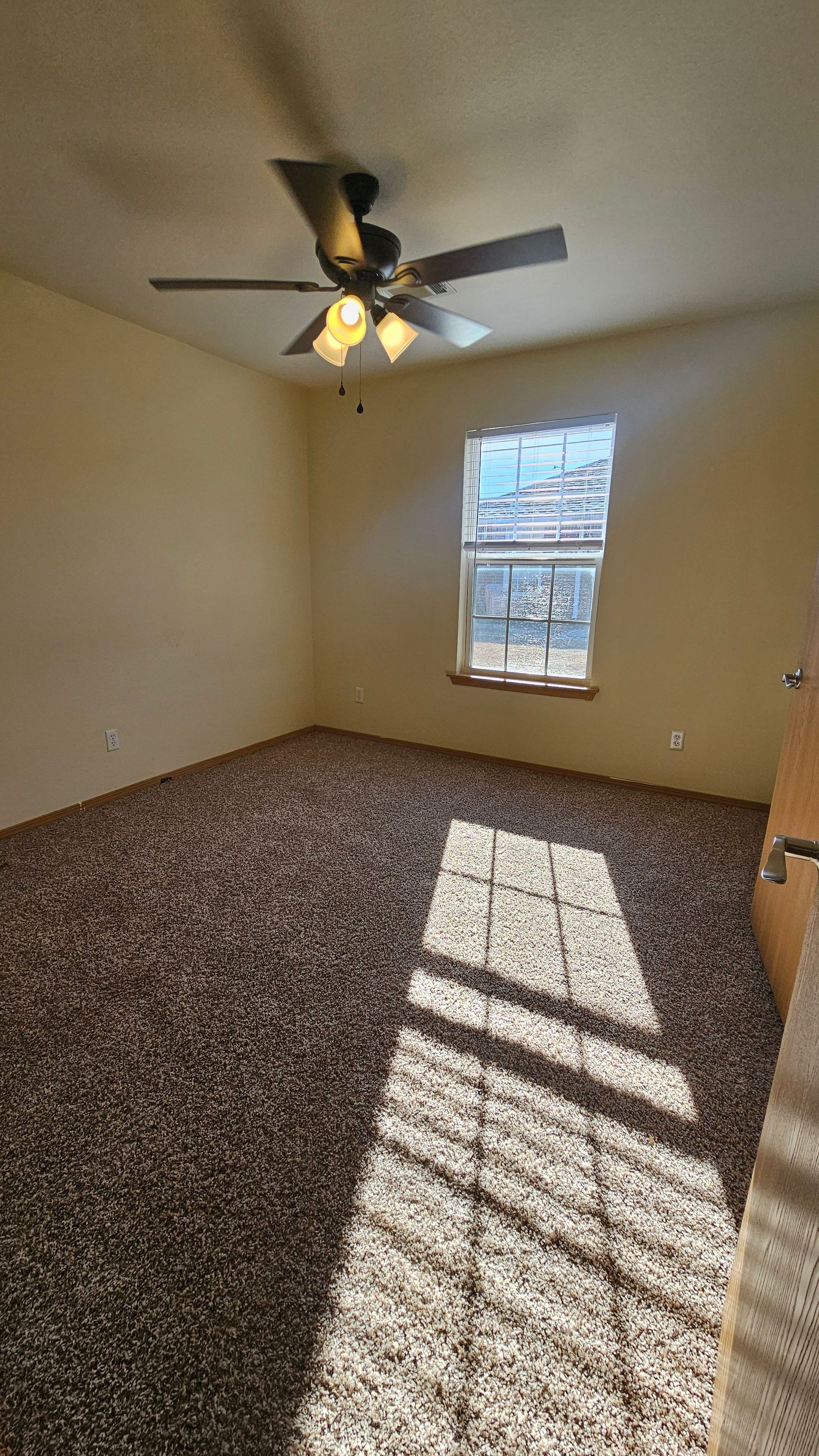 An empty bedroom with a ceiling fan and a window.