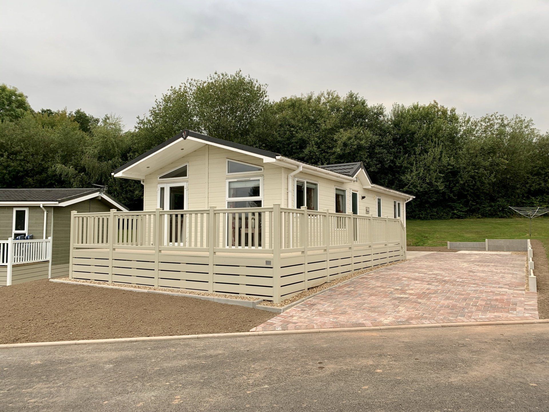 A white mobile home with a large deck is sitting on top of a dirt field.