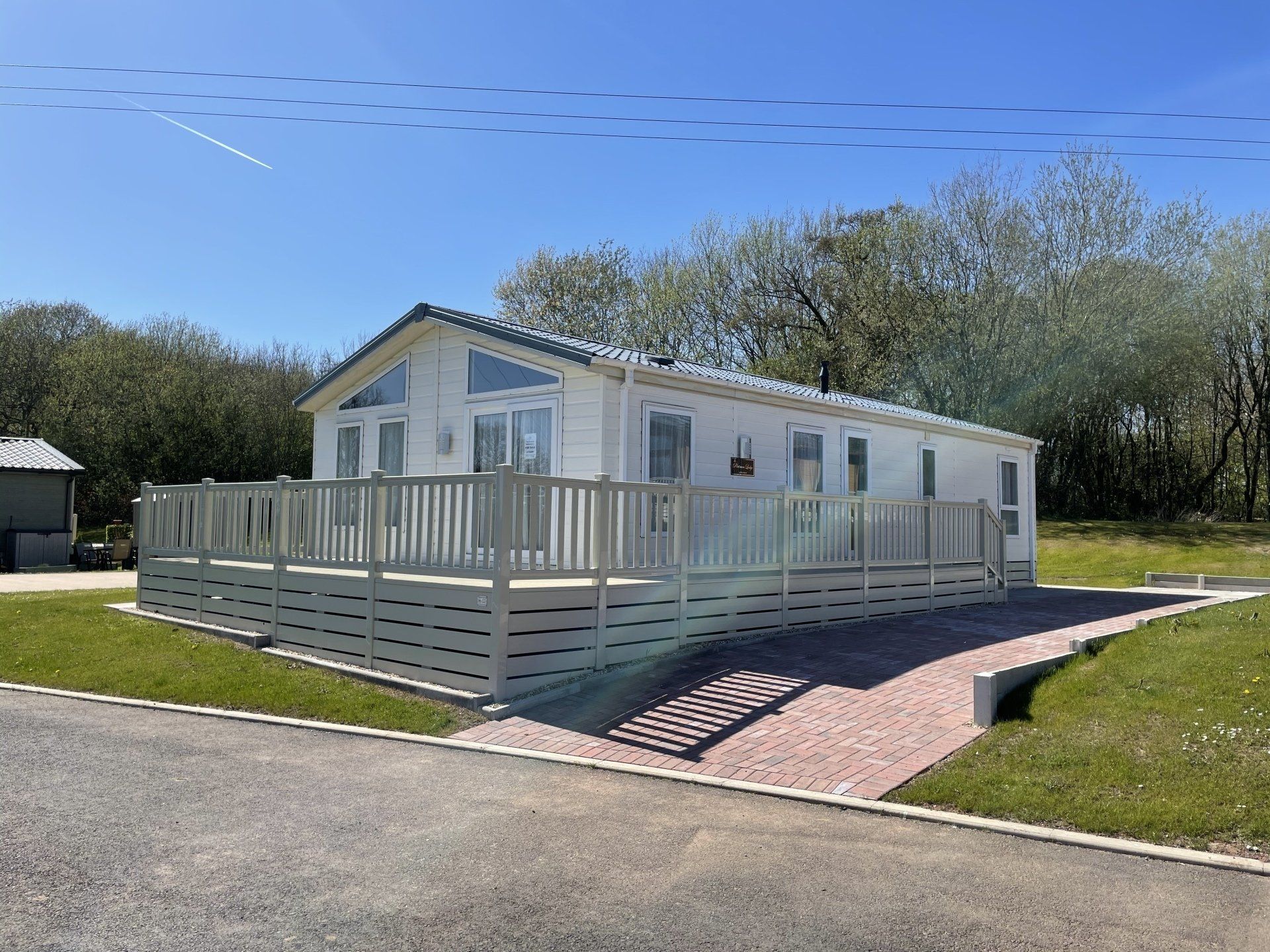 A mobile home with a large deck is sitting on top of a lush green field.