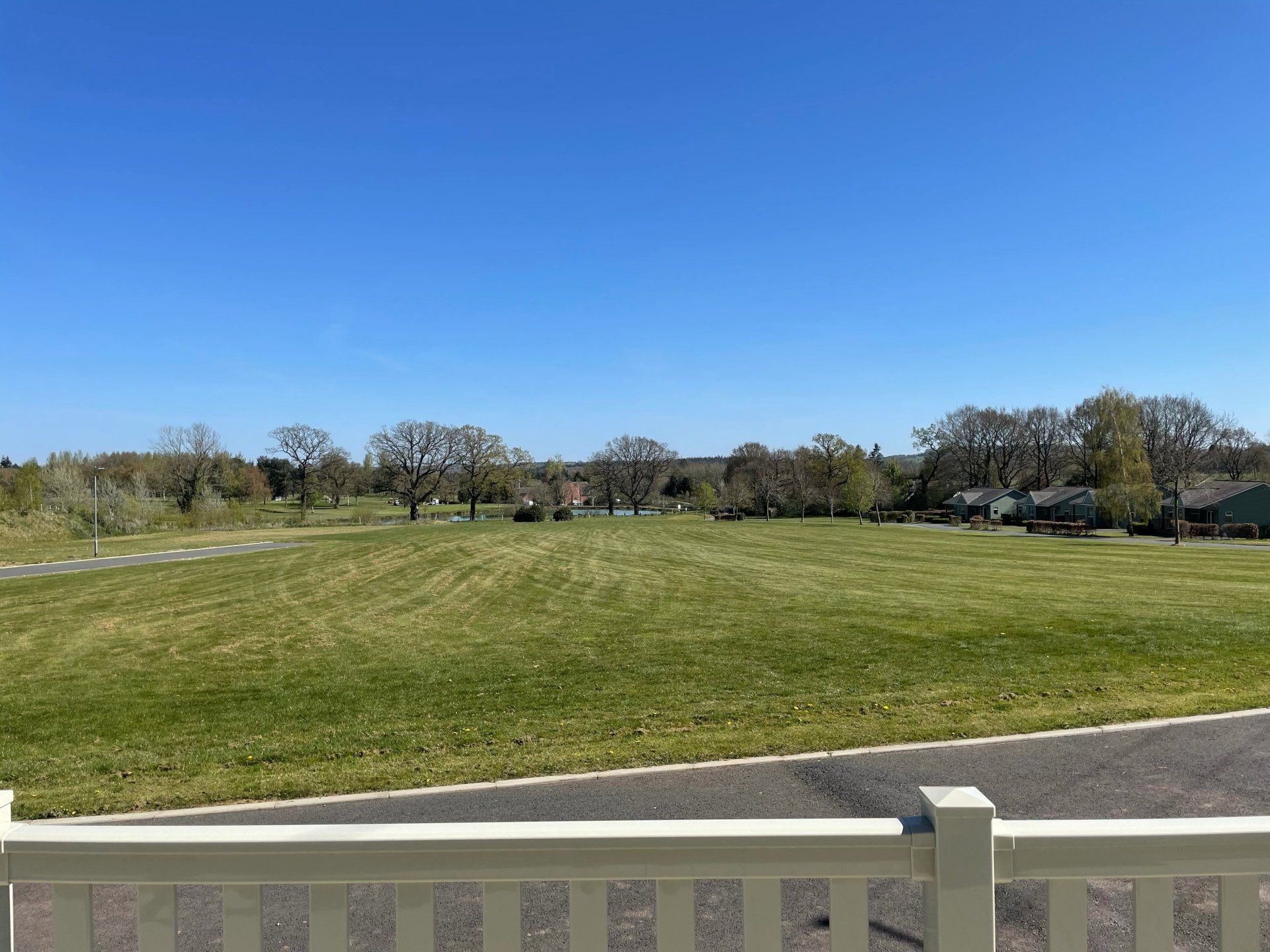 A view of a grassy field from a balcony with a white fence.