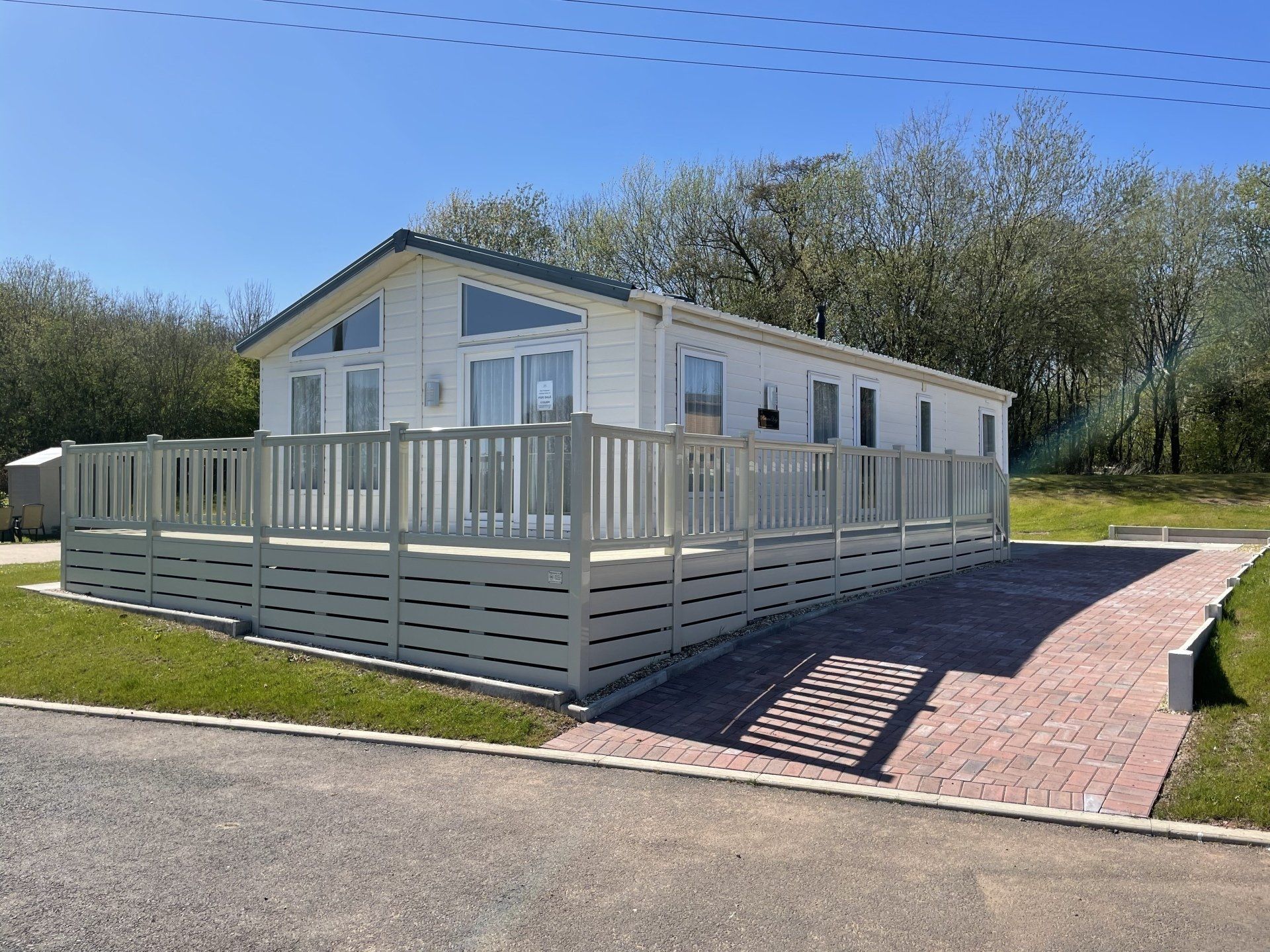A white mobile home with a large deck and a brick driveway.