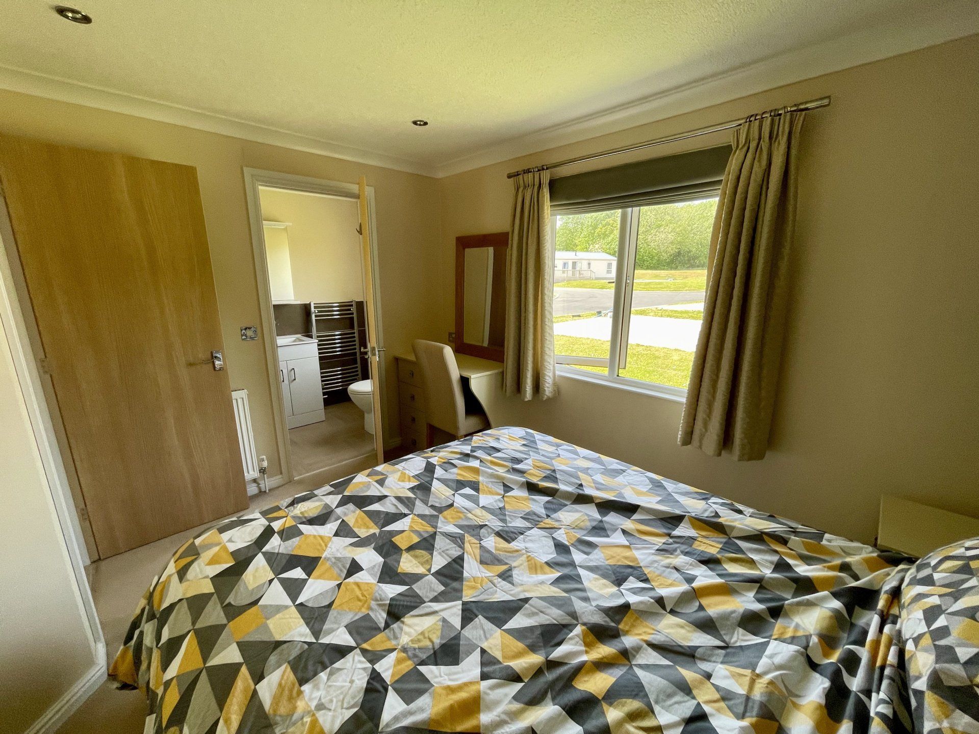 A bedroom with a bed , dresser , mirror and window.