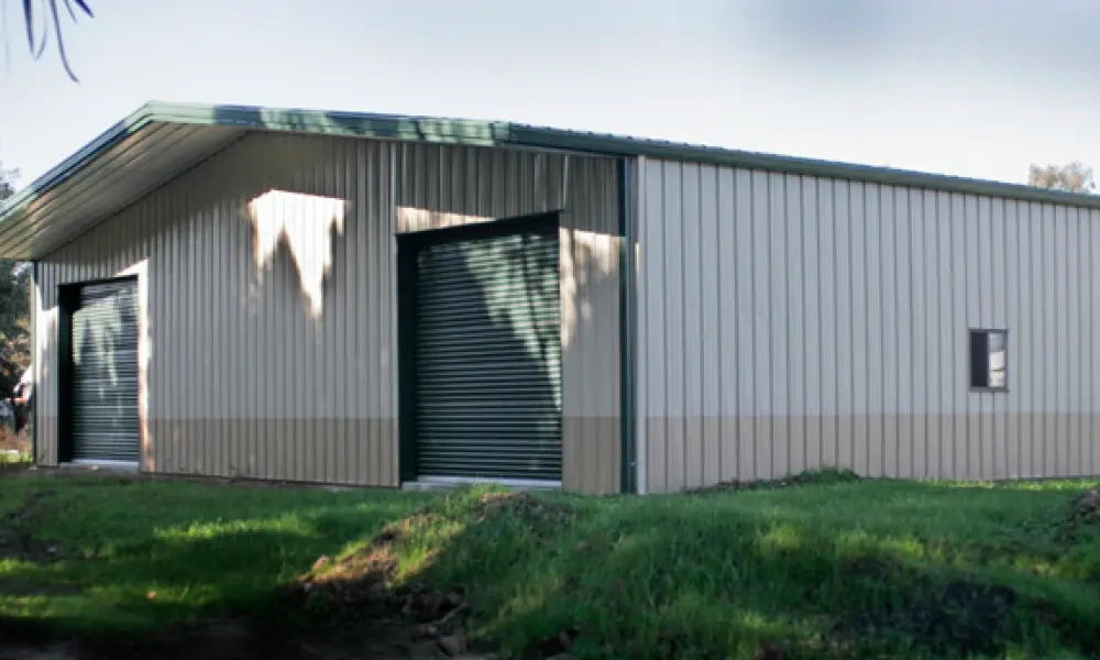 A large metal building with a green roof is sitting in the middle of a grassy field.