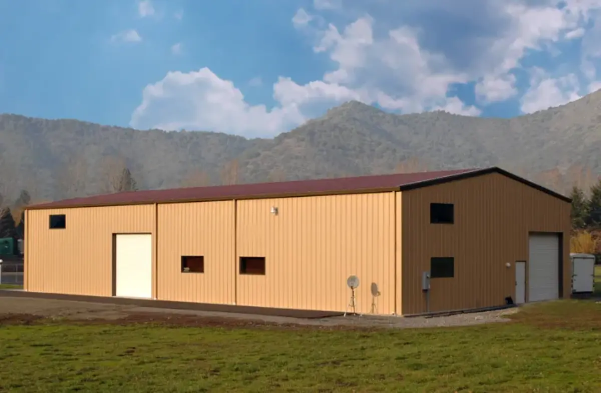 A large building is sitting in the middle of a grassy field with mountains in the background.