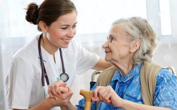 Un'infermiera tiene la mano di una donna anziana su una sedia a rotelle.