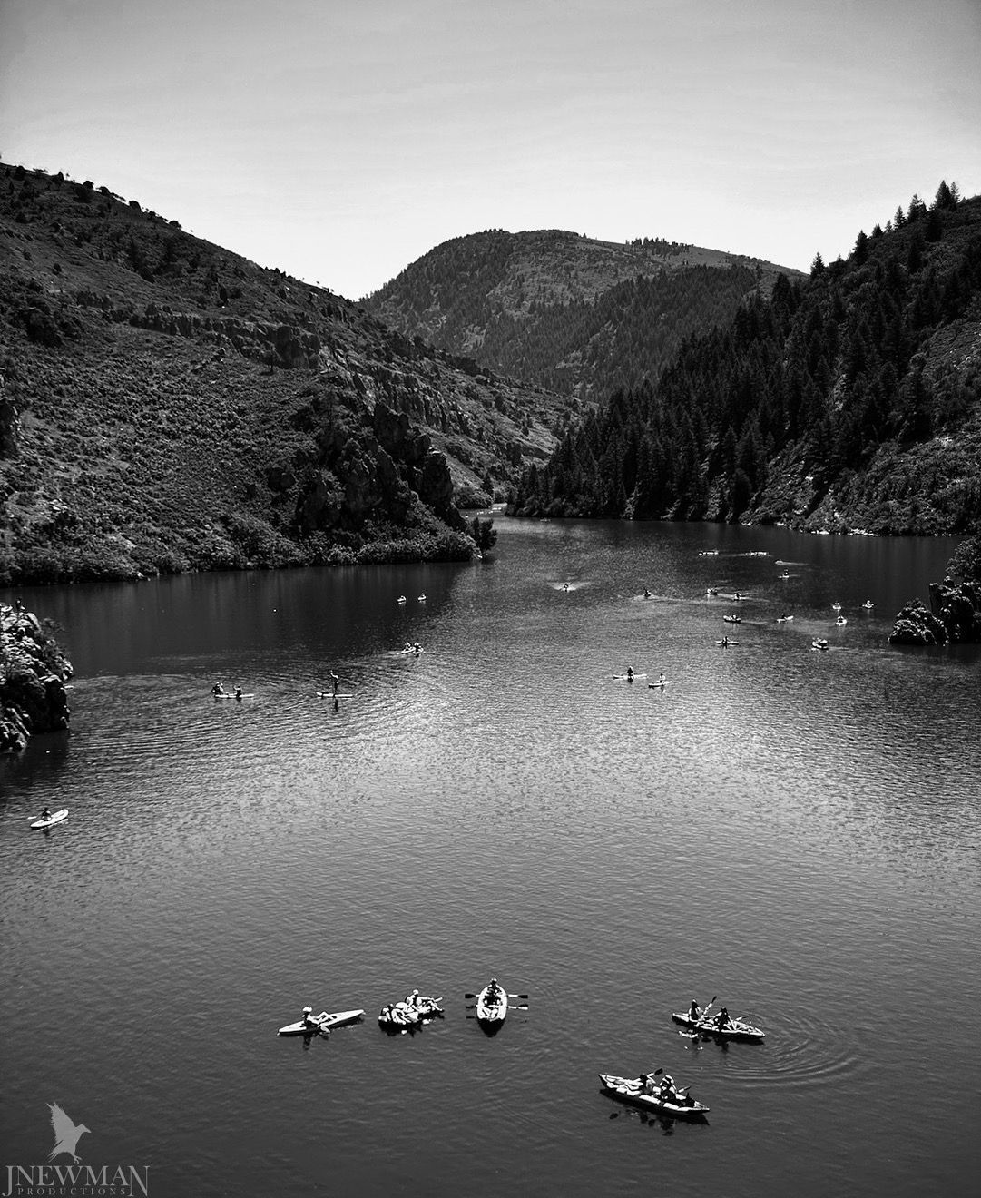 Black and white photo of boats on a lake surrounded by forested hills.