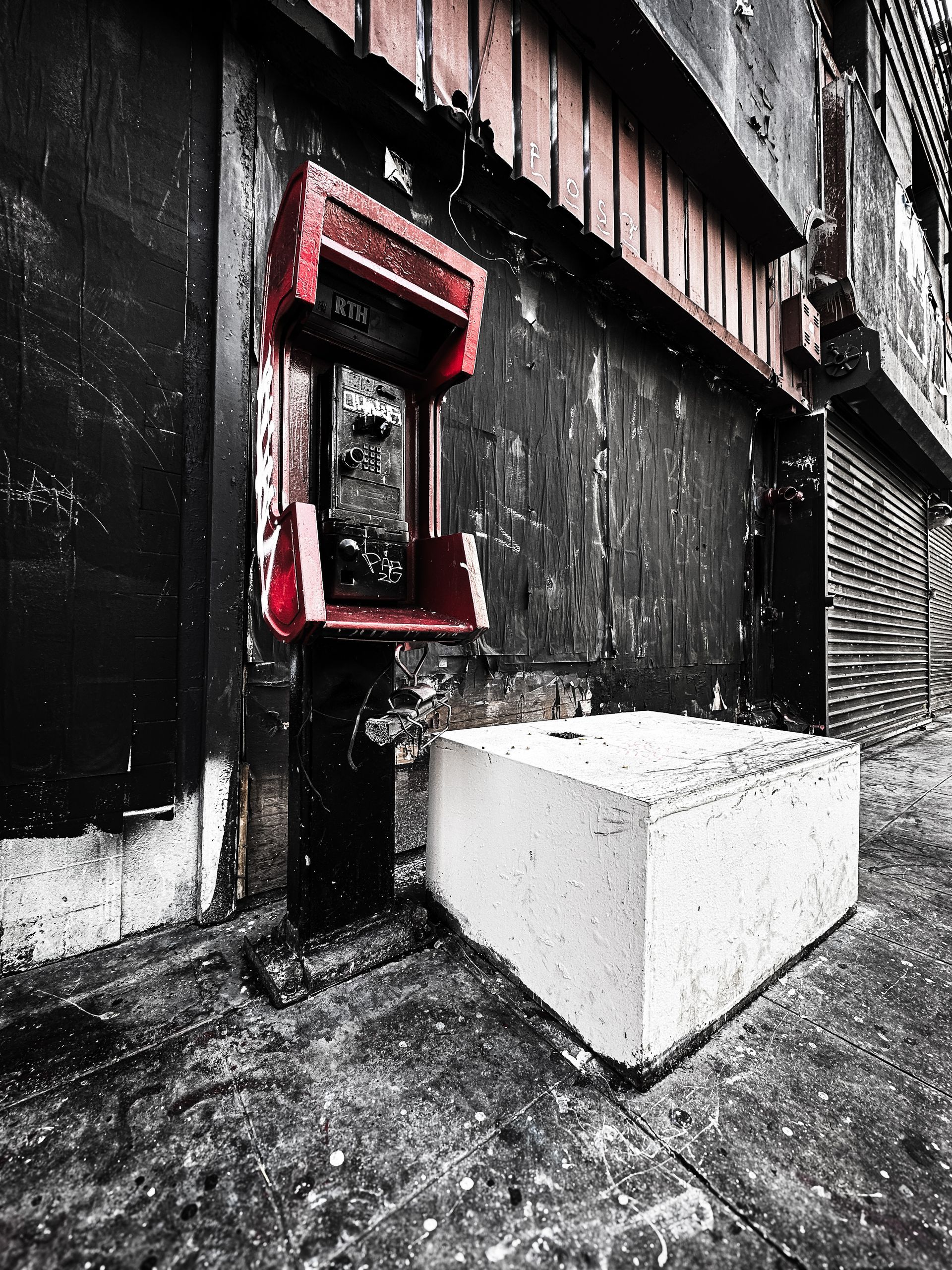 Red payphone against a weathered black wall, a white concrete block in front.