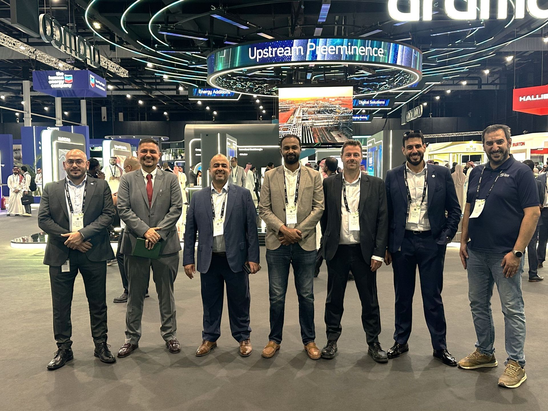 Group of men in suits and business casual attire, posing inside a conference center.