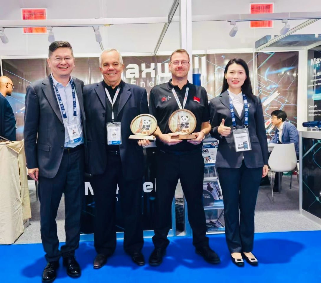 Four people holding awards at a trade show booth, smiling. Two men hold awards; a woman gives a thumbs-up.