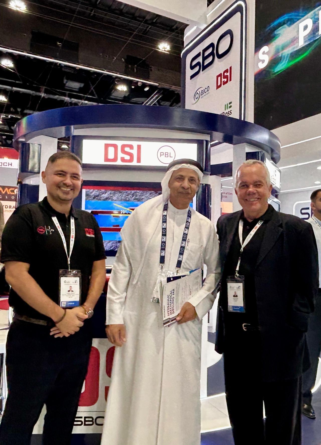 Three men pose at a trade show booth,