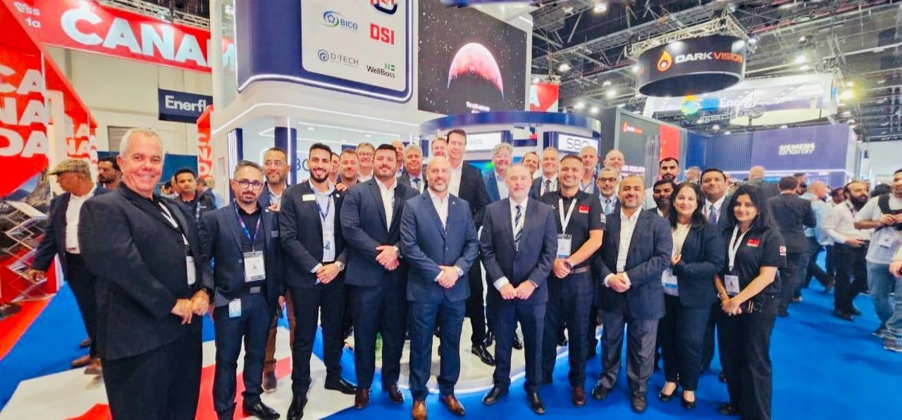 Group of people in suits posing together at a trade show booth with the word