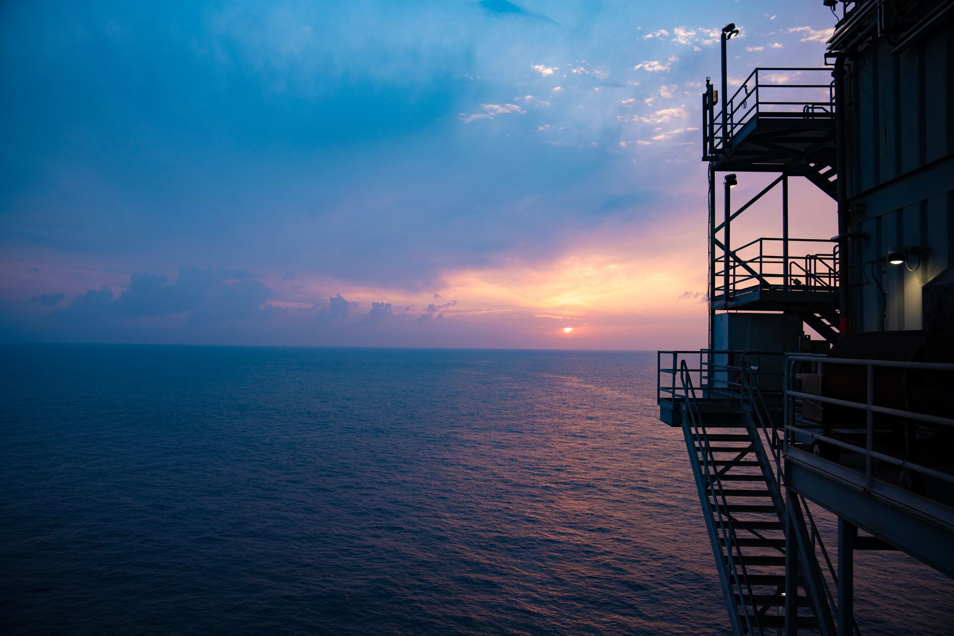 A staircase leading up to a building overlooking the ocean at sunset.