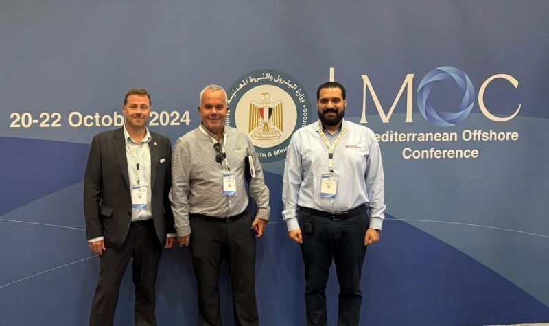 Three men are standing in front of a wall that says mediterranean offshore conference.
