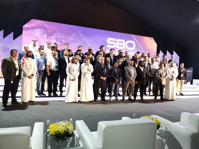 A group of people are posing for a picture in front of a stage with the word sbo on it.