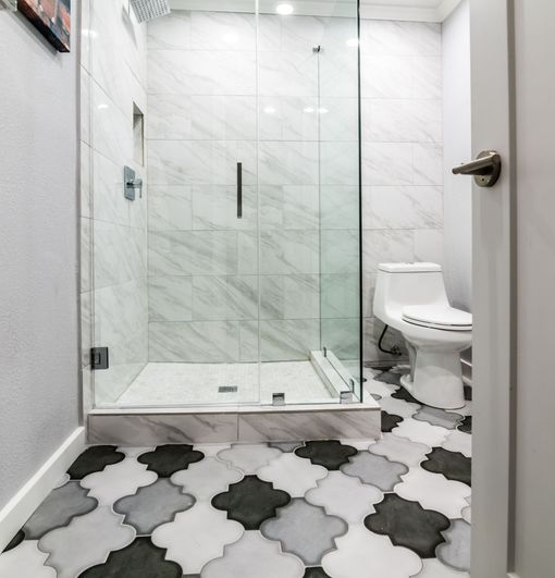 Modern bathroom with glass shower, white marble tile, and black-and-white patterned floor