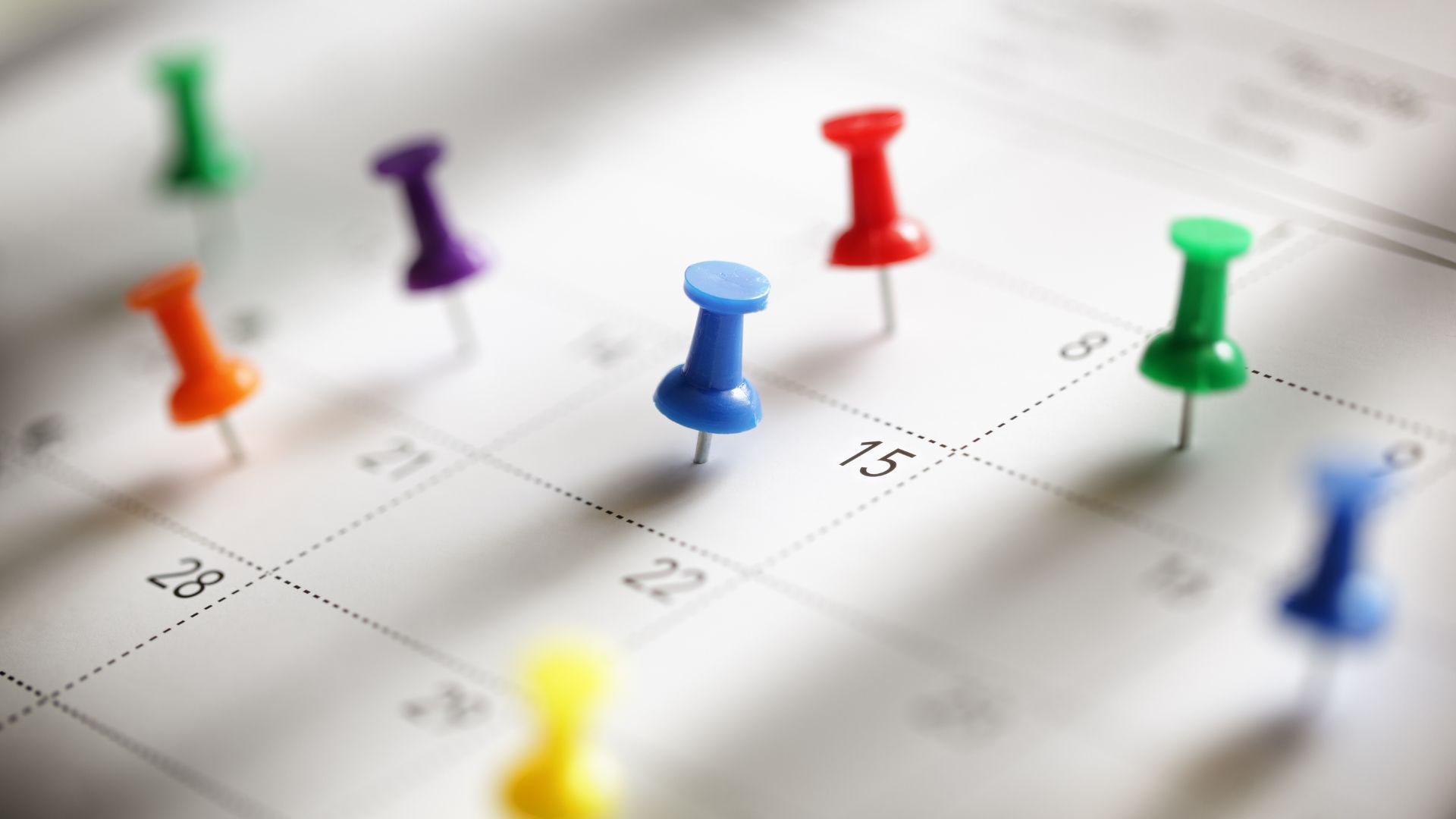 Calendar with colorful push pins marking dates.