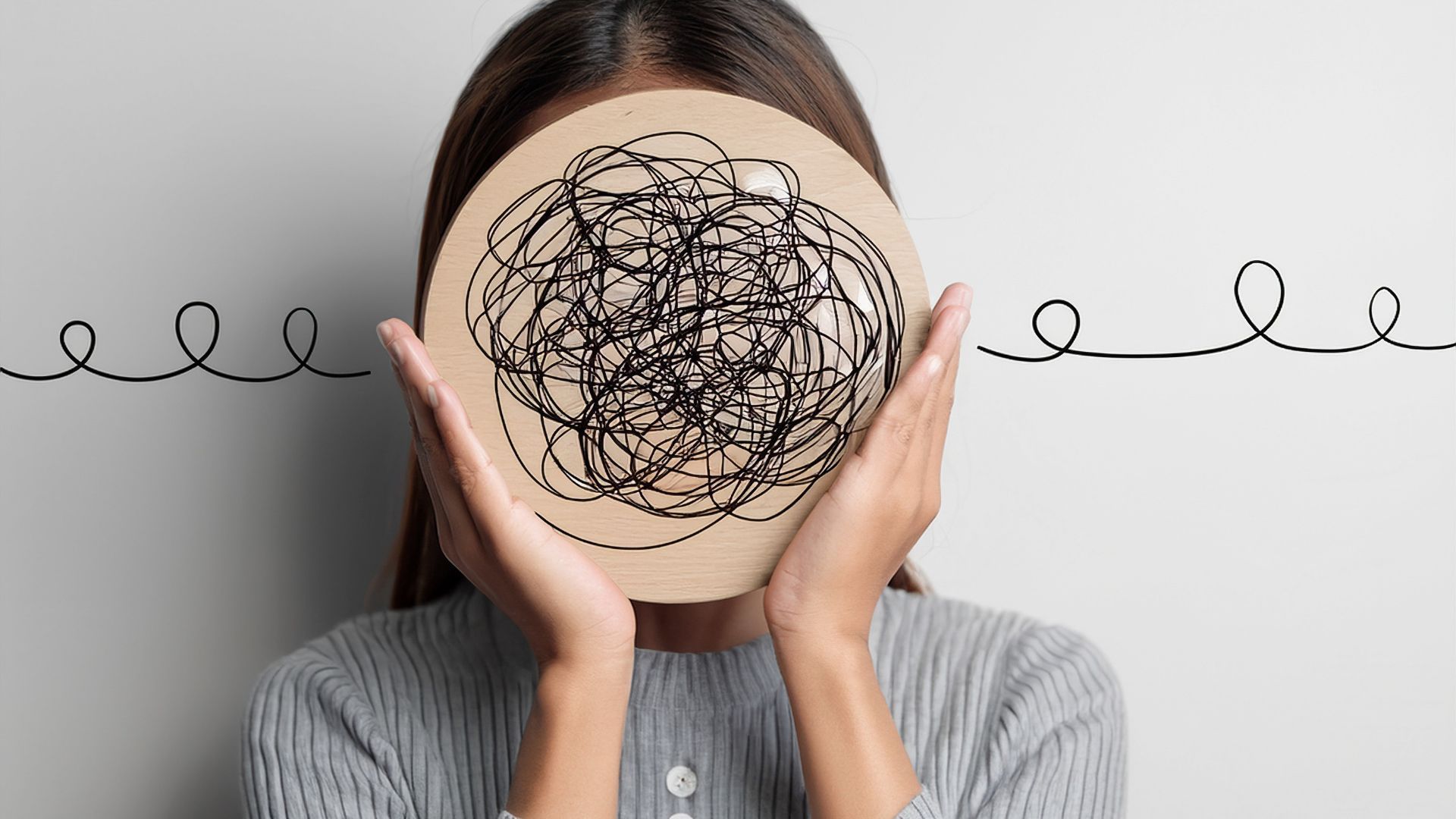 A person holds a circular board with a chaotic black scribble over their face, with squiggly lines extending to the sides.