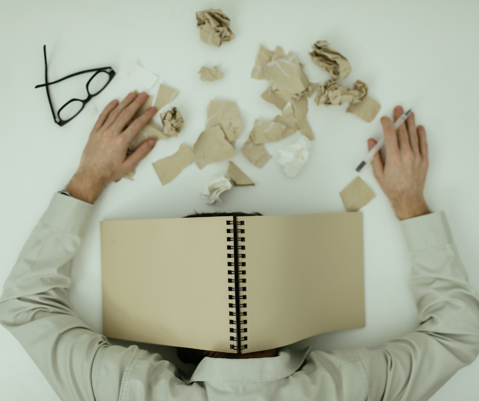 Man with head on desk and book over his head because he is exhausted
