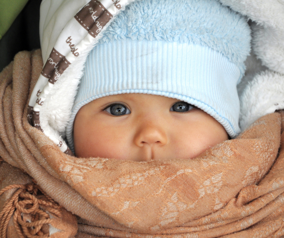 Baby wearing light blue winter hat and brown scarf, bundled up warmly.