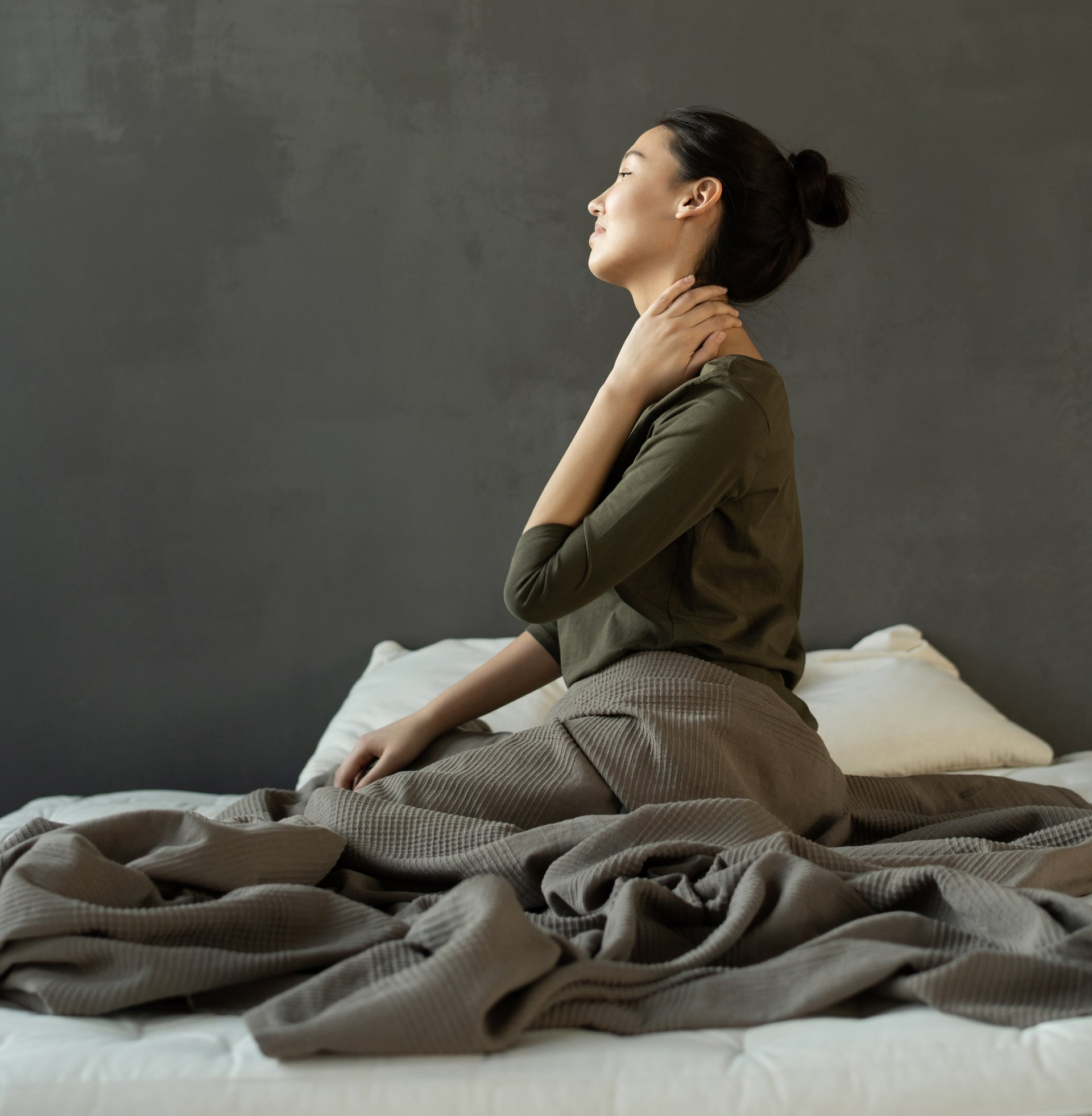 A person with dark curly hair sleeps in a bed wearing a gold satin eye mask, resting their head on a white pillow.