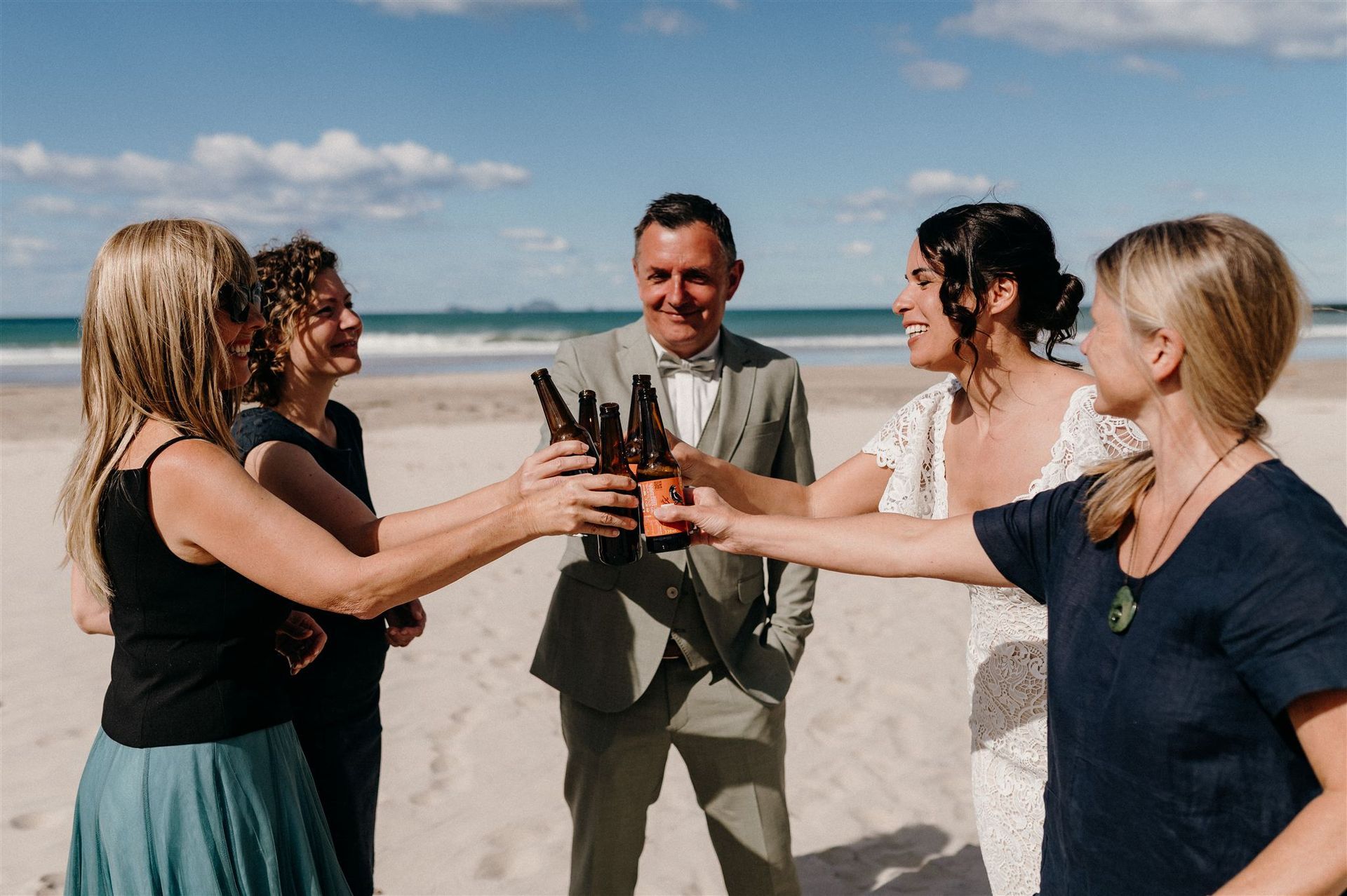 Brautpaar, Trausprecherin und Trauzeugen stoßen an einem sonnigen Strand an und lächeln bei einem fröhlichen Toast.