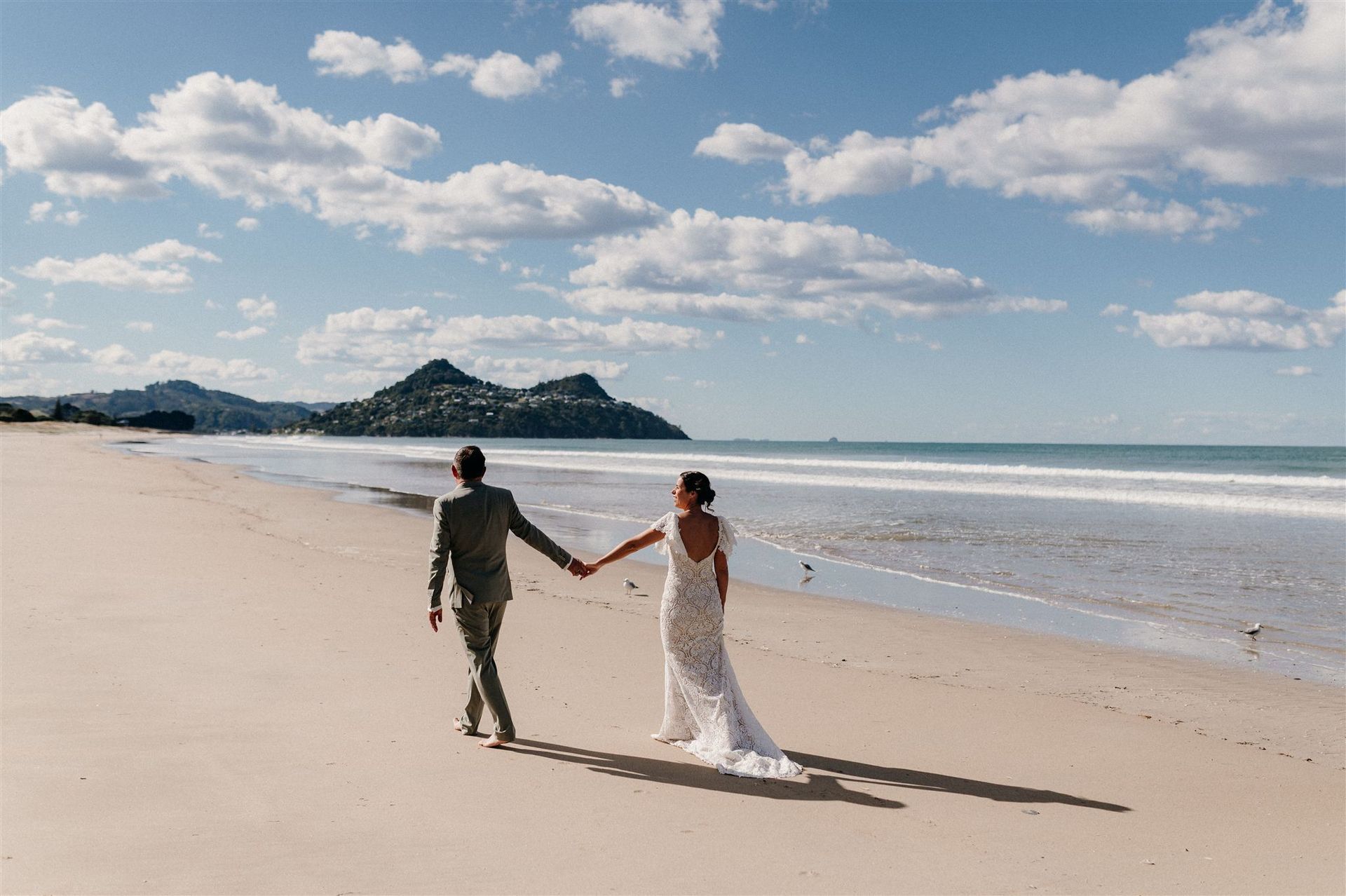 Brautpaar geht einen weissen, endlos langen Sandstrand entlang für den die Coromandel Peninsula so berühmt ist