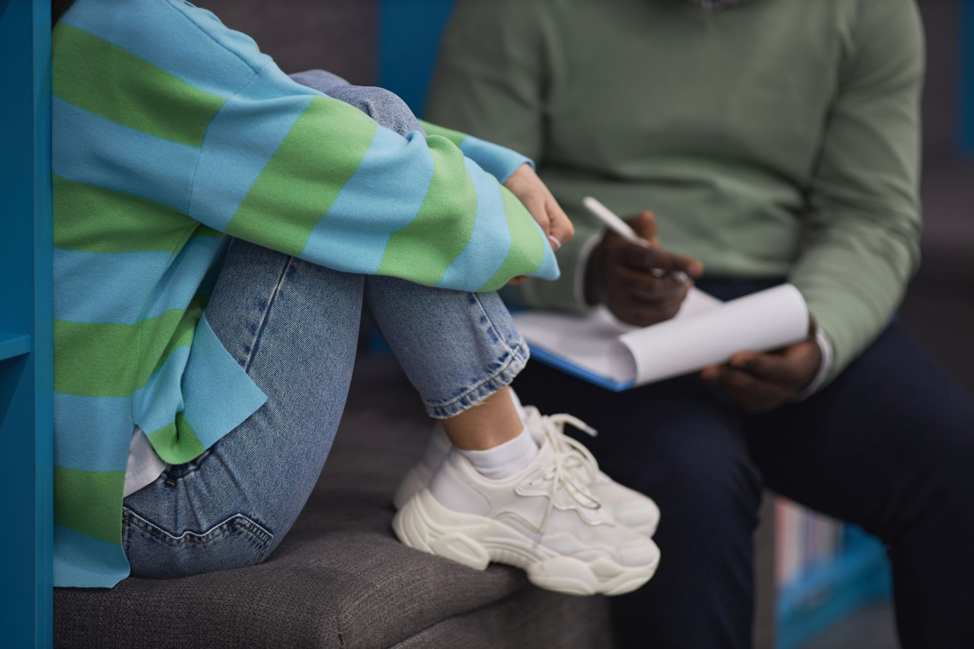 A woman is sitting on a couch with her legs crossed while a man writes on a clipboard.