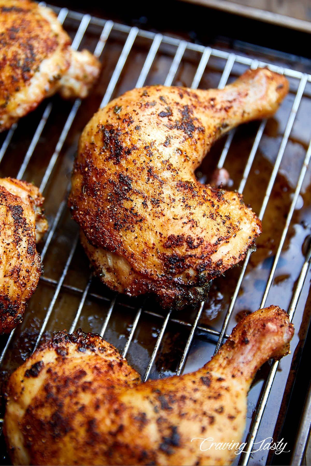 Three chicken legs are sitting on a wire rack on a pan.