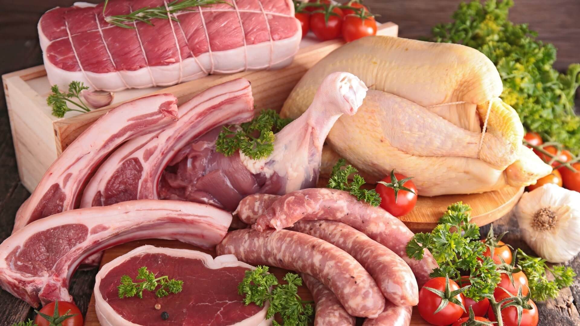 A variety of raw meats and vegetables on a wooden table.