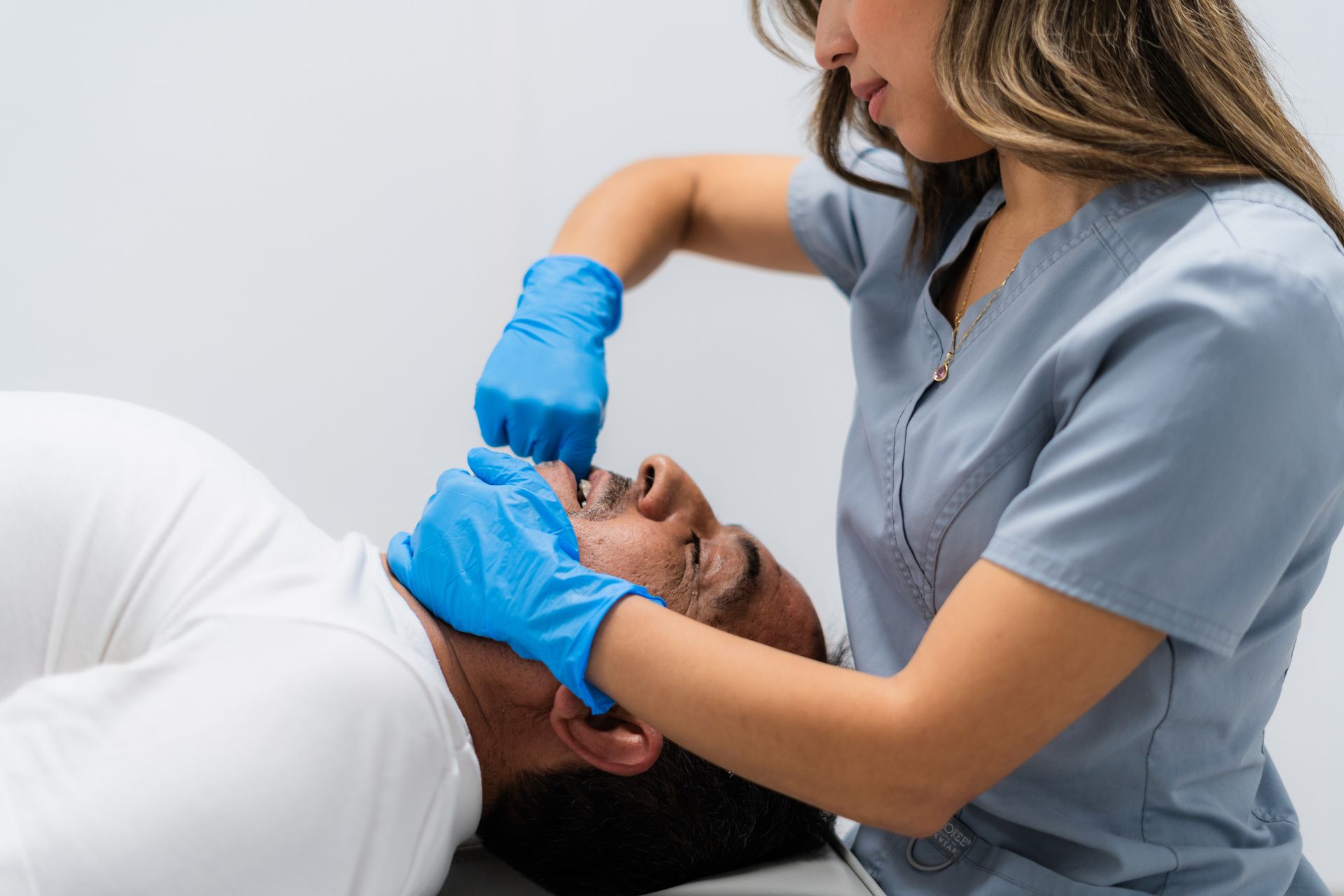 A chiropractor performing a jaw adjustment on a reclining patient.