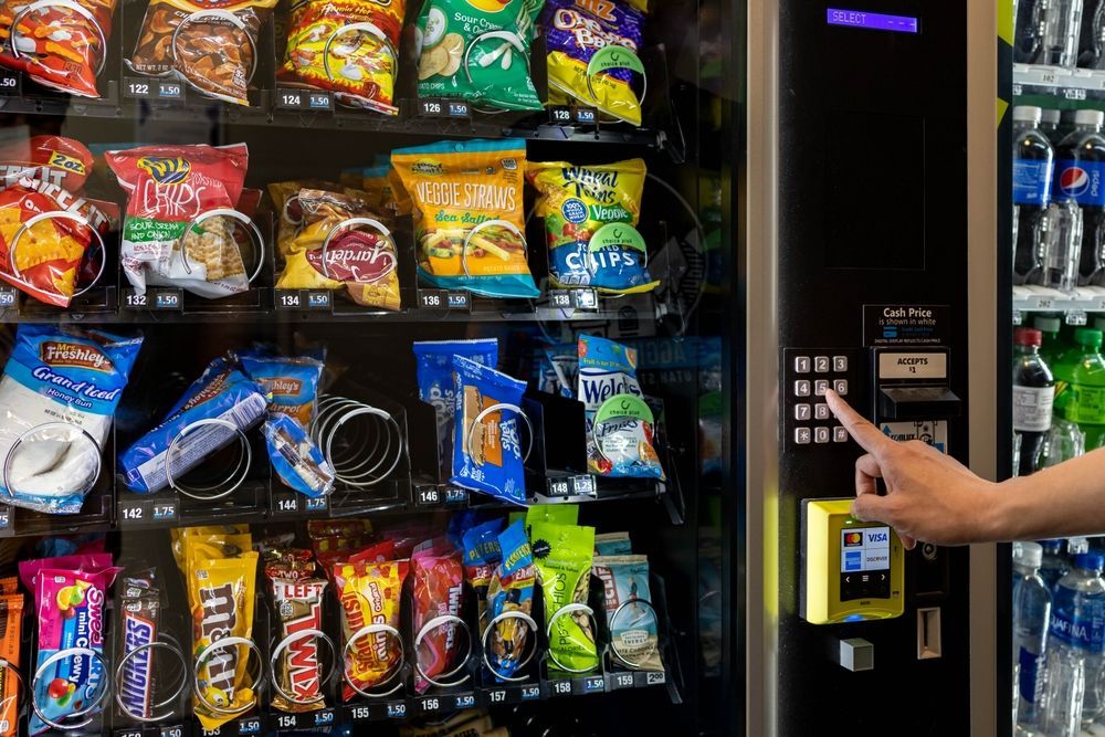 Hand selecting a snack from a vending machine filled with chips, candy, and drinks.
