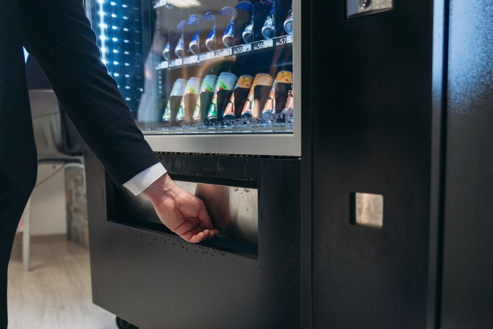 Person reaching into a black vending machine to retrieve a purchased item.
