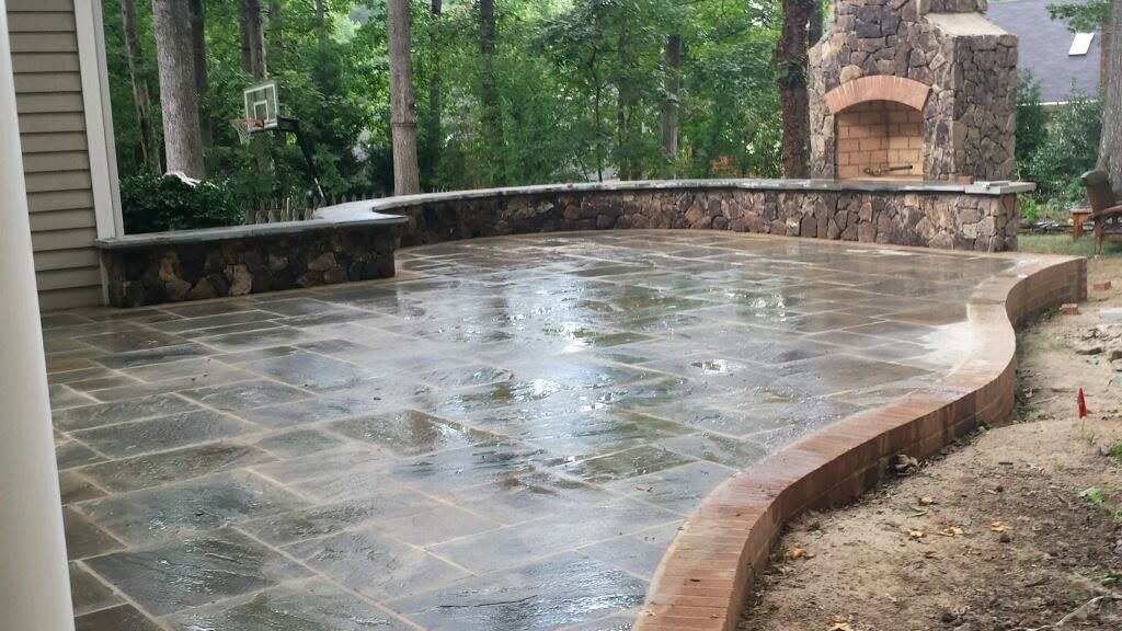Wet stone patio with curved brick edging beside a wooded yard during rain