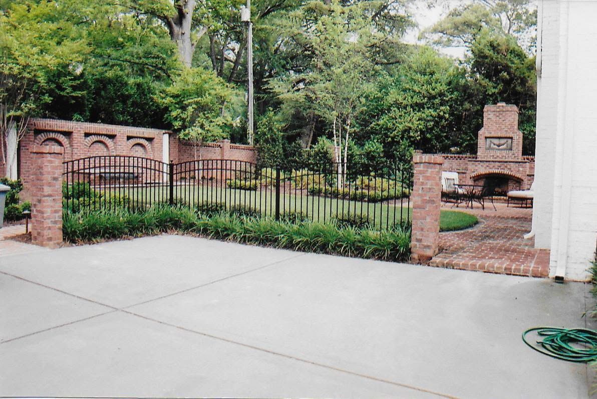 Brick-and-iron gated entrance with greenery and a sidewalk in front