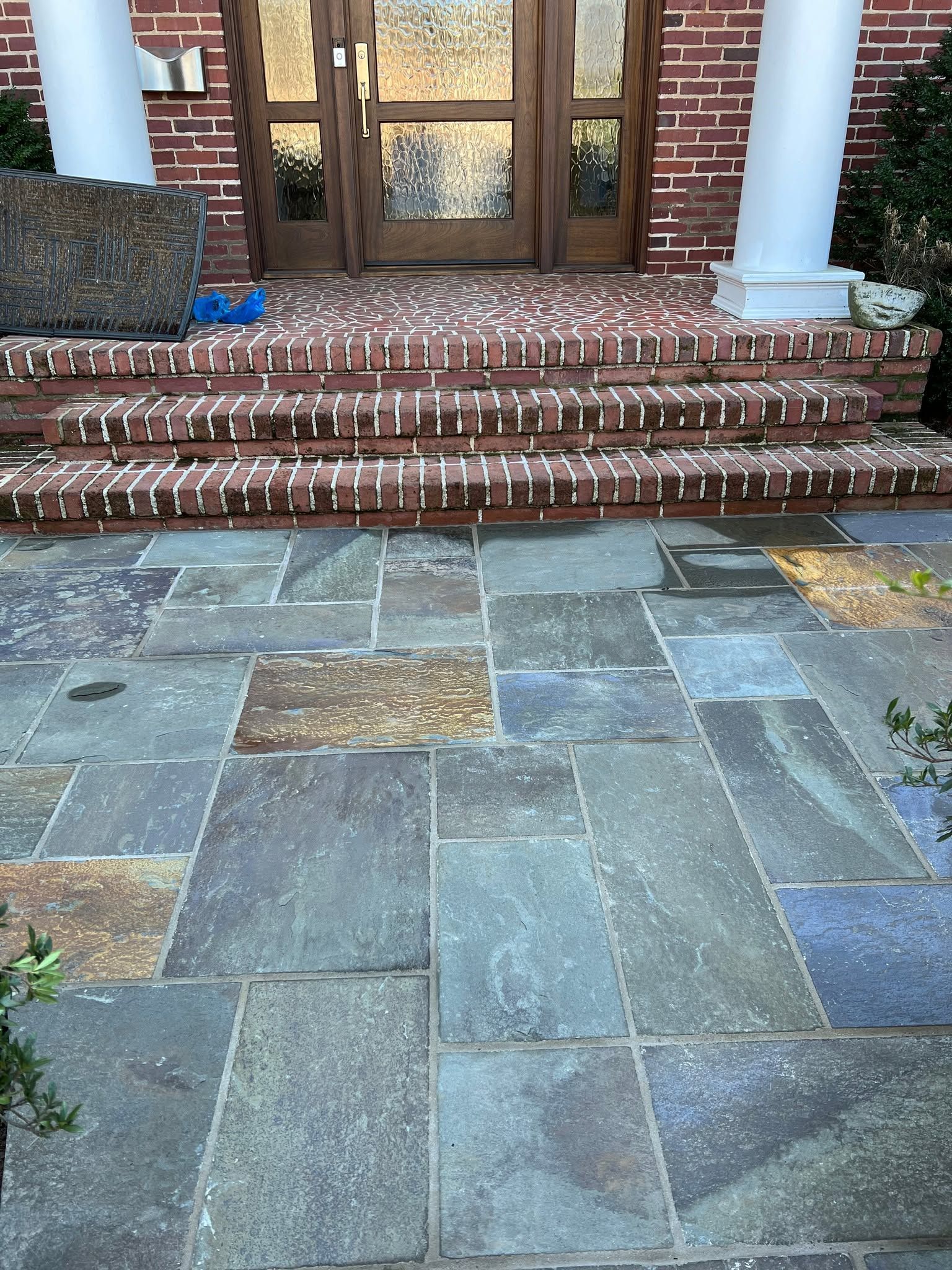Brick front steps leading to a wooden double door, with stone walkway and white columns.