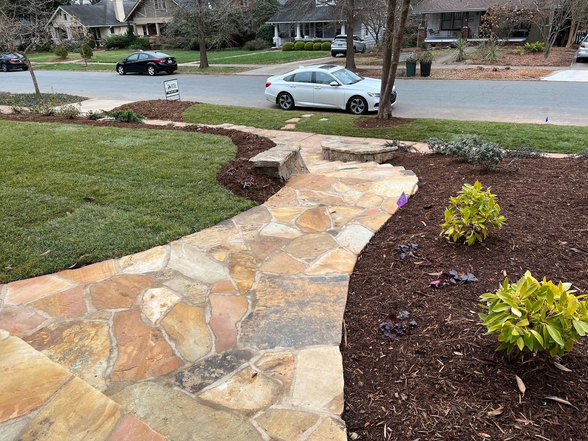 Stone garden path through landscaped front yard toward a suburban street with parked cars